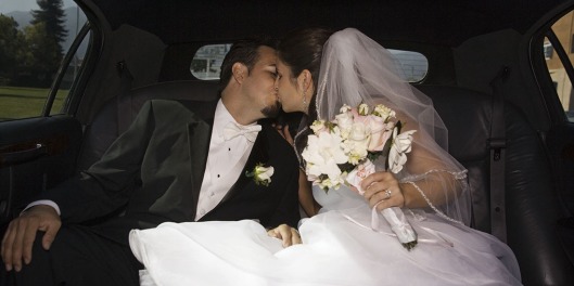 Hispanic newlyweds kissing in limousine